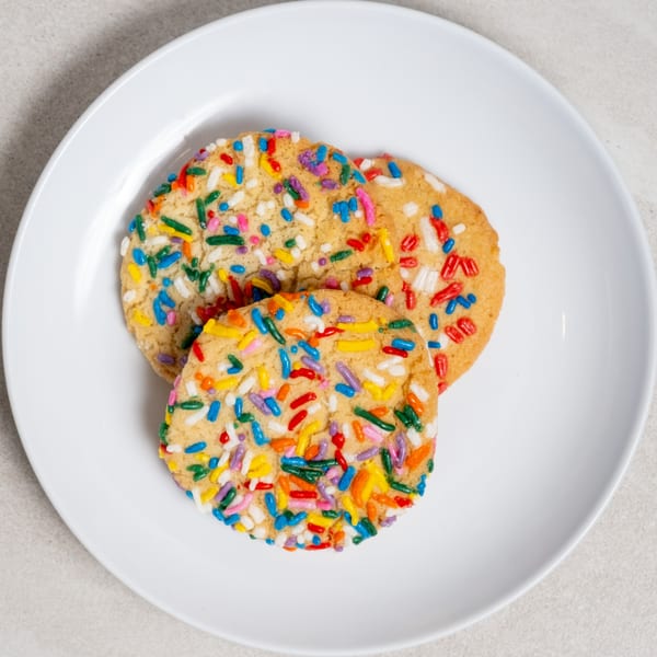 Three round sugar cookies with colorful sprinkles on a white plate.