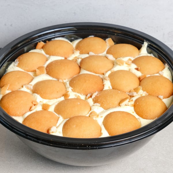 A large black bowl filled with banana pudding, topped with vanilla wafers and crumbs.
