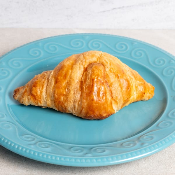 Golden-brown croissant from Sweet Valentine Bakery, perfectly baked and resting on a blue plate.