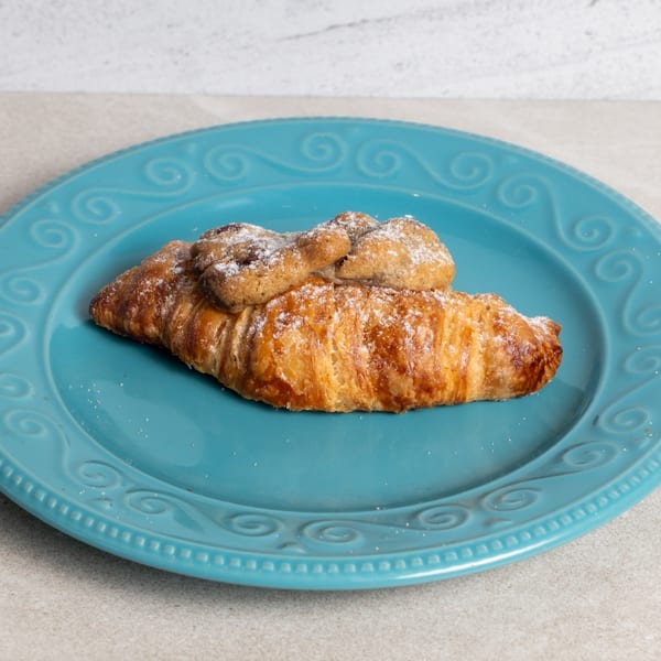 A golden-brown croissant topped with two small, powdered sugar-dusted cookies on a blue plate.